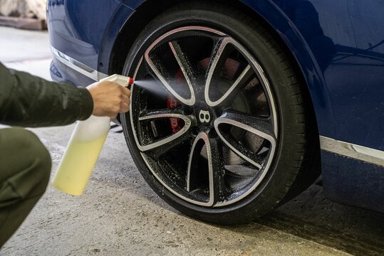 Young man washing a car, using car shampoo to clean the rims.