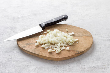 Wooden board with chopped onion and a knife on a light gray background, top view. Cooking delicious homemade food