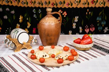 Rustic table with a jug, decorative barrel, cheese roll-ups, cherry tomatoes, and red peppers.