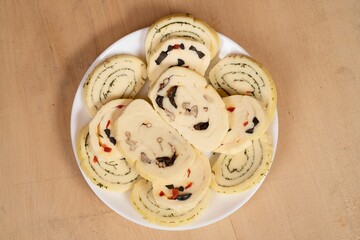 Closeup of a plate with cheese roll-ups on the wooden table.