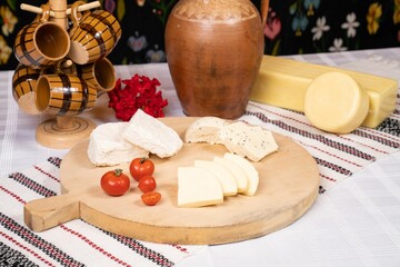 Closeup of a dining table featuring a variety of cheeses, tomatoes, and a decorative jug.