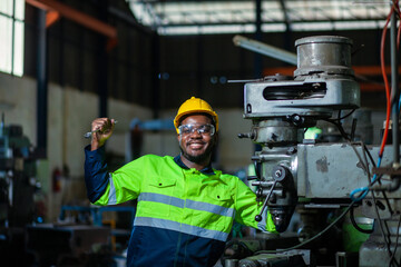 Portrait of an African American engineer standing with his arms crossed, inspecting and controlling an automated welding robot. The robotic arm in the automotive factory is smart.