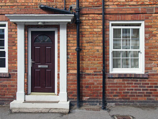 Fototapeta na wymiar front view of a typical old small english terraced brick house with black painted door and white portico and windows