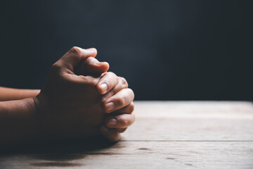 Hands folded in prayer on a Holy Bible in church concept for faith, spirituality and religion,...