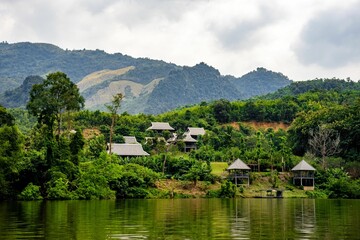 Fototapeta premium a river near some small buildings surrounded by green trees and mountain in the distance