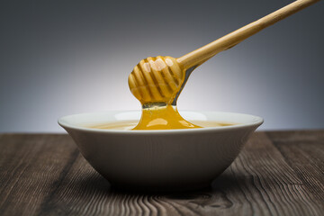 honey drips from the spoon into a white bowl