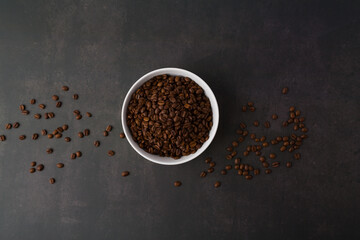 Coffee beans in the white bowl. Top view. on dark stone background.