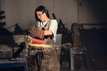 Focused female blacksmith cutting metal
