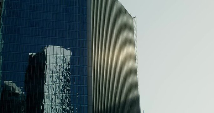 The glass facade of a modern skyscraper with other high-rise buildings reflected in the windows