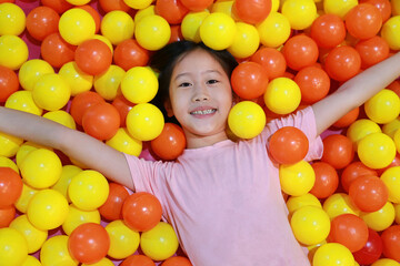 Fototapeta na wymiar Cheerful Asian girl child playing at colorful plastic balls playground.