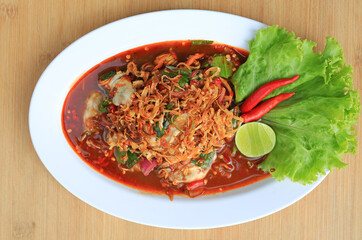 Oysters in spicy salad in white plate against wood background. Thai style food. Top view.