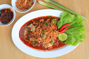 Oysters in spicy salad in white plate served with Chili Paste and fried onions against wood background. Thai style food. Top view.