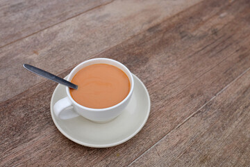 Tea with milk in porcelain cup on wood table background.