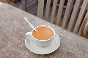 Tea with milk in porcelain cup on wood table background.