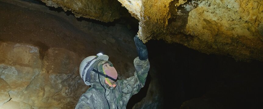 Scientist exploring of cave for geology science. Professional speleology worker in helmet carry out visual inspection on underground nature. Engineer check stalactites.Preservation of earth resources