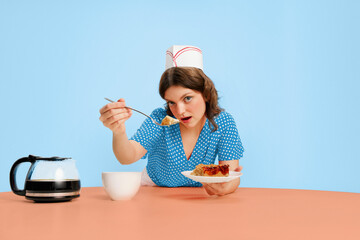 Stylish young female waitress in retro american fashion style of 70s, 80s sitting at table and drinking coffee over grey background. Funny meme emotions, ad, sales. Trash pop art