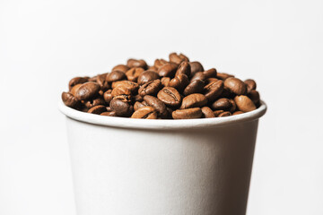 Paper cup filled with grains of fried coffee on white background.