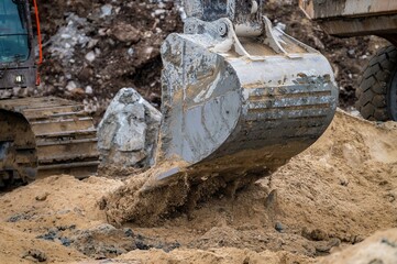 Close-up image of an excavator bucket emptying sand, motion