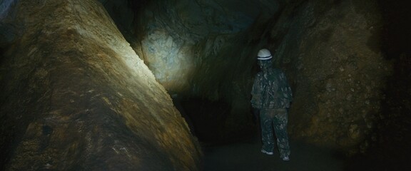 Professional speleology worker in helmet carry out visual inspection on underground nature. Preservation of earth resources. Engineer check stalactites.Scientist exploring of cave for geology science