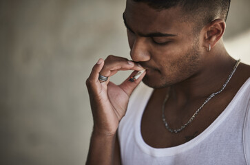 Getting high just to get by. a young man smoking a marijuana cigarette against an urban background.