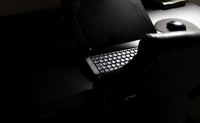 Notebook with keyboard and mouse on a black desk with a chair for home office
