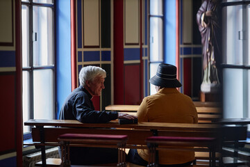 Rear view of senior priest talking to visitor while they sitting on bench during ministration in...