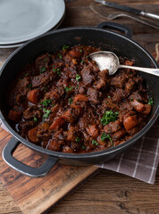 Braised pork with carrots and gravy in a pot on wooden table