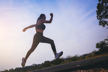 Silhouette of young woman running sprinting on road. Fit runner fitness runner during outdoor workout with sunset background.