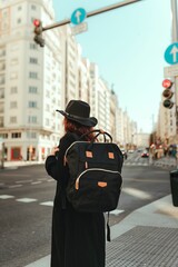 Vertical back view of a young female wearing black coat and backpack on the street