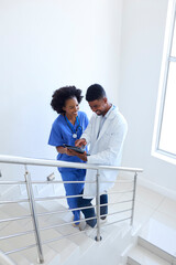 Male Doctor And Female Nurse With Digital Tablet Discussing Patient Notes On Stairs In Hospital 