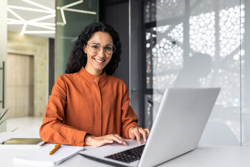 Fototapeta na wymiar Young beautiful hispanic woman working inside modern office, businesswoman smiling and looking at camera at work using laptop