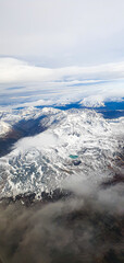 Fototapeta premium Flying over the Andes Mountains with sparse clouds and below the white immensity of snow.