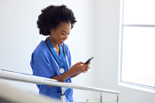 Female Doctor Or Nurse Browsing On Mobile Phone On Stairs In Hospital 