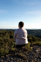 No binary reflecting on the edge of a large rock, at his feet an immense landscape of Somontano forests, light pink long-sleeved thin T-shirt, very short hair, overweight