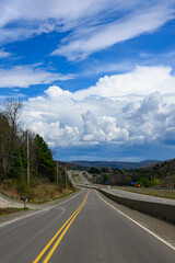 Fototapeta premium Driving down the old route with the new highway just to the left of me. The road seems to be heading right into the clouds ahead. A beautiful white fluffy cloud over the horizon in Windsor NY.
