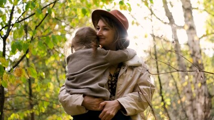 Hello September. A young mother in a brown hat and a little daughter walk in the city park in autumn. Mom holds the girl in her arms and hugs her tightly with love.