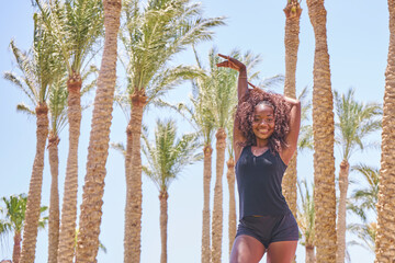 Portrait of african beautiful and sexy girl in T-shirt and shorts smiles in the summer vacation against a backdrop of palm trees.         