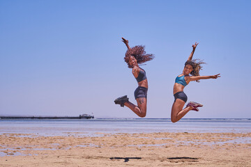 Happy bikini two women jumping of joy and success on perfect white sand beach on tropical vacation. Holiday girls with sexy slim suntan body running of freedom