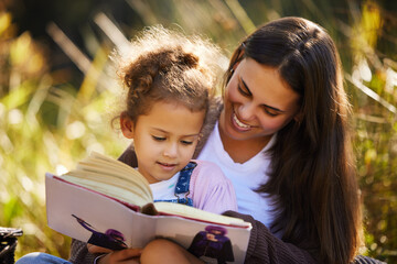 Stretch your imagination. an attractive young woman reading to her daughter while picnicking in the...