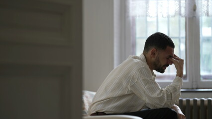 Dramatic moment of One man suffering alone sitting on couch feeling frustration and desperation during difficult times