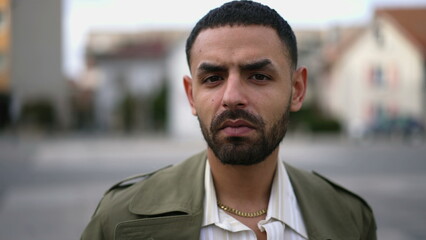 Closeup face of a serious Middle Eastern man looking at camera standing in urban environment