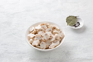 Fresh chopped mini champignons and spices: bay leaf, black pepper on a light gray table, cooking homemade vegan food