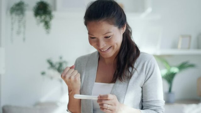 Video of happy woman celebrating while looking at predictor finding out she is pregnant at home