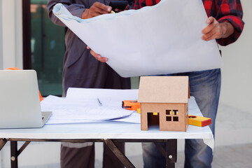 House model on desk over confident team of architects working together in a office. Architect discuss with engineer about project in office, architectural concept.