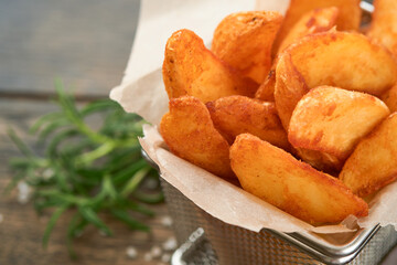 French fries in metal wire basket with salt and ketchup on old wooden dark background clous up. Fried potatoes. Fast food and unhealthy food concept.