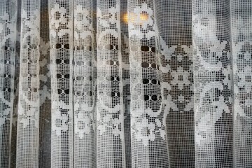 Altmodische weiße transparente Gardinen mit Blumenmuster hinter Glasscheibe von Fenster mit goldgelbem Licht 