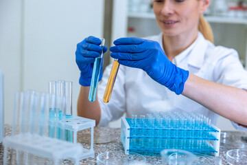 Woman biologist holds test tubes with yellow and blue liquids in hands doing experiments in biology