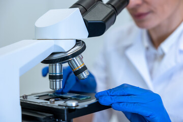Unrecognizable female scientist looking petri dish with genetically modified sample under microscope