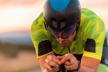  Close up photo of triathlete riding his bicycle during sunset, preparing for a marathon. The warm...