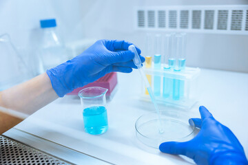 Unrecognizable scientist holding test tube with reagent, dropping color liquid over glass equipment.